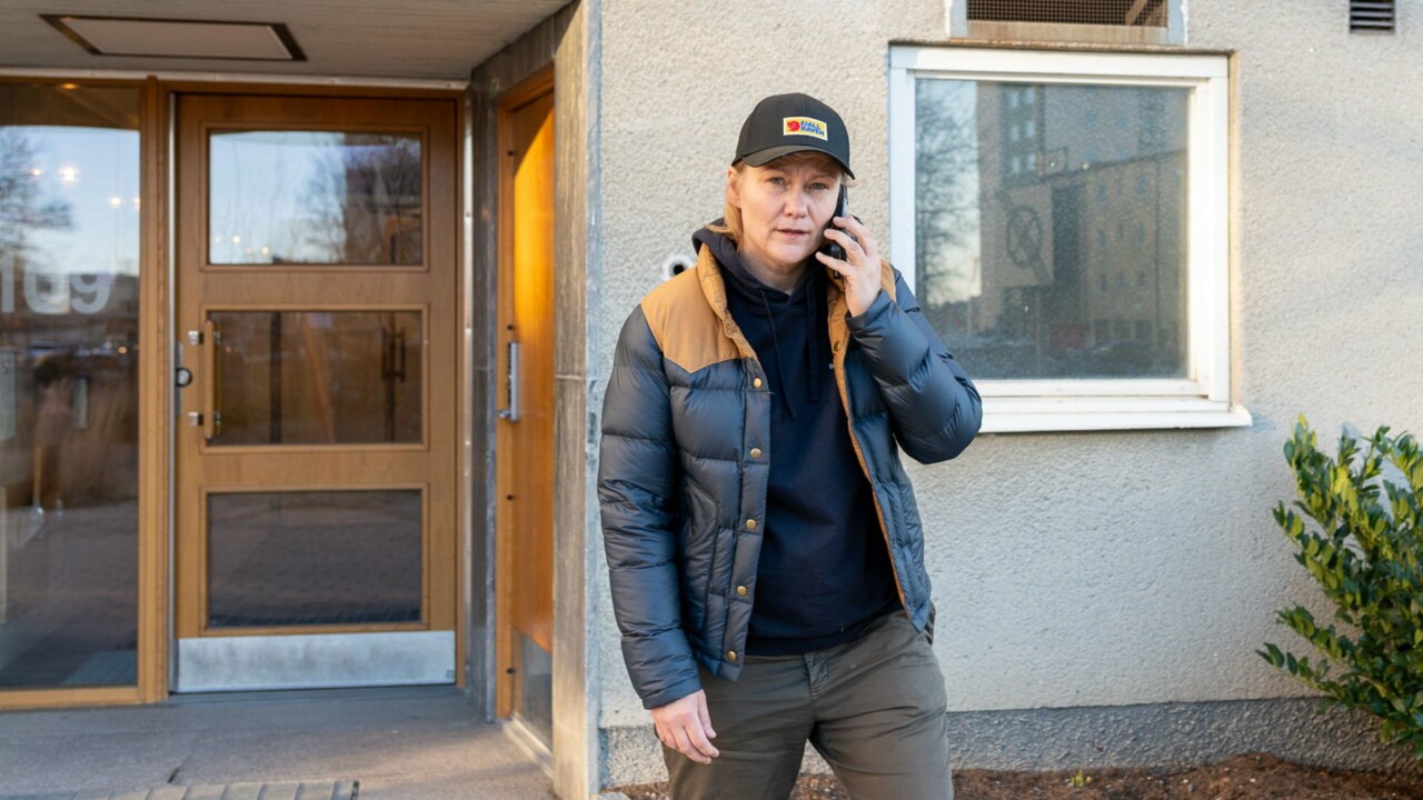 En kvinna går ut från sin port och pratar i mobiltelefonen.