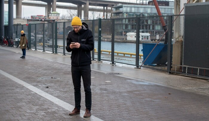 En man står utomhus med mobilen i händerna.