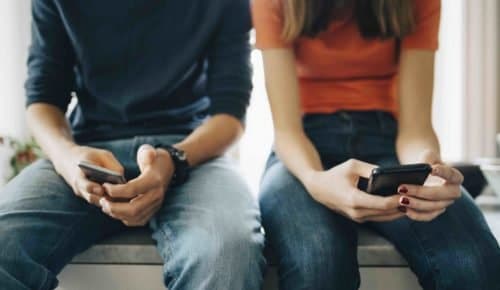 Två tonåringar sitter på köksbänk med varsin mobilelefon i knät. Prata nakenbilder och dickpics med din tonåring