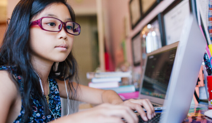 Flicka sitter framför en laptop och skriver på tangentbord. Internetkunskap