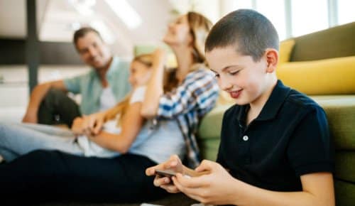 Barn sitter med sin familj och kollar på en mobiltelefon