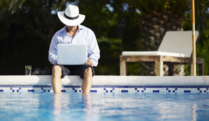 Man med hatt med dator och fötterna i poolen. Se Netflix utomlands