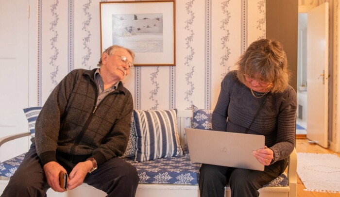 Äldre par som sitter i en soffa. Mannen kikar på datorn som kvinnan har i knät.