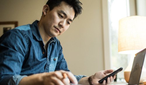 Bilden visar en man som arbetar med sin dator och mobiltelefon.