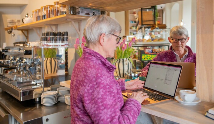 Äldre kvinna surfar på sin dator på ett cafe