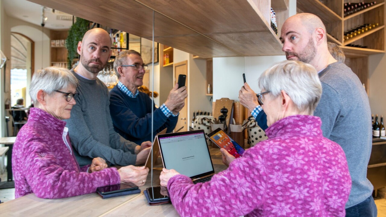 Människor i blandade åldrar står med varsin skärm på ett cafe
