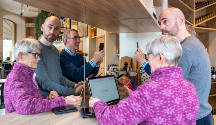 Människor i blandade åldrar står med varsin skärm på ett cafe