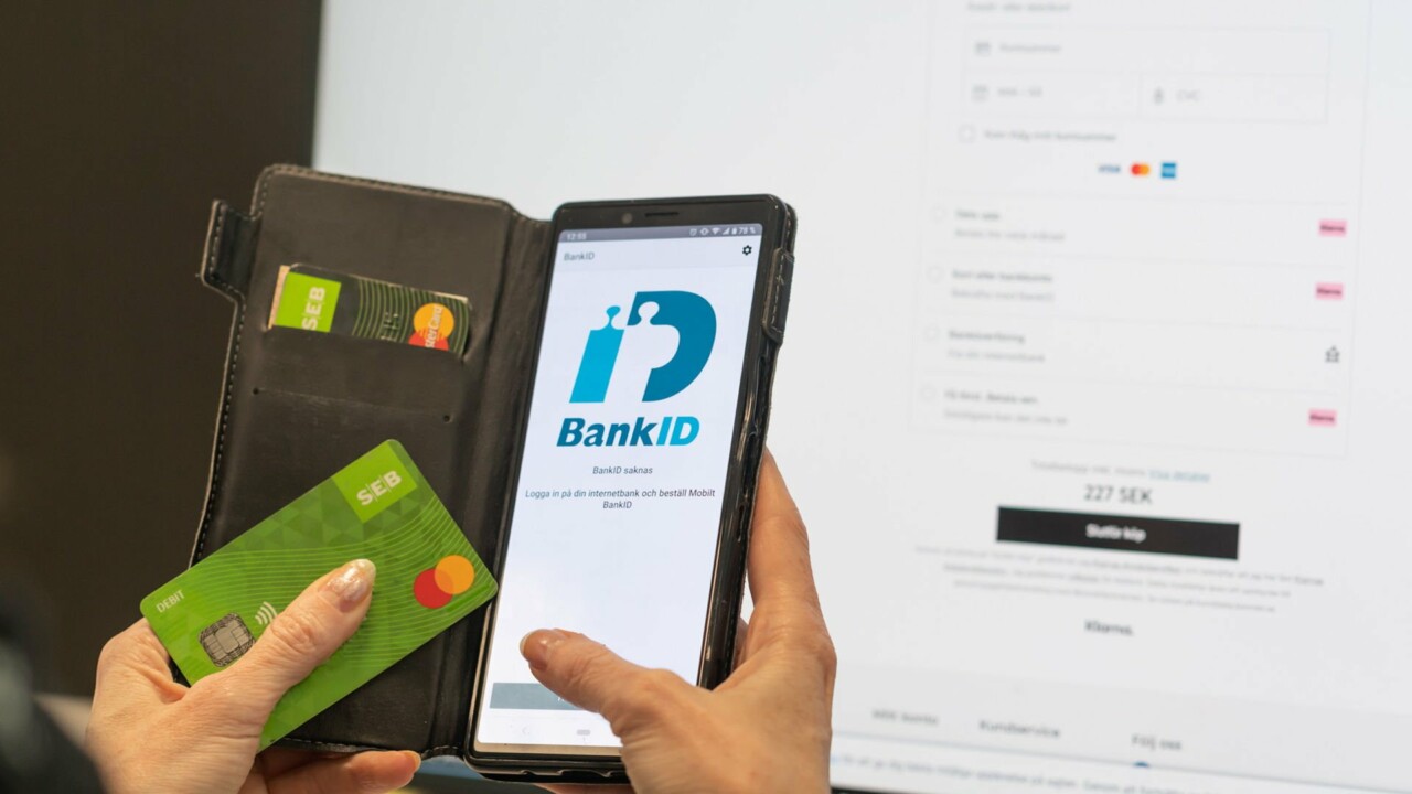 Någon håller i en mobil med bank-id på skärmen och ett kreditkort i andra handen.