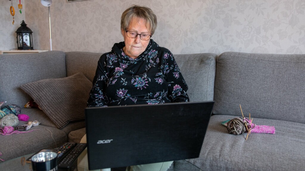 En kvinna sitter i soffan med en laptop framför sig, hon ser aningen bekymrad ut.