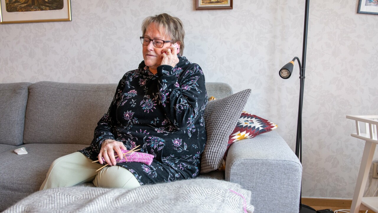 En äldre kvinna sitter i sin soffa och pratar i mobiltelefonen