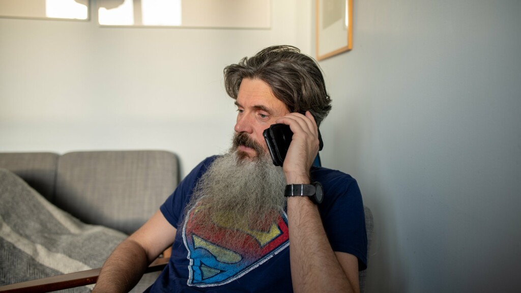 Man med skägg sitter i en soffa och pratar i smartphone