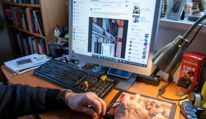 En äldre person sitter vid en dator med sociala medie-konto på skärm framför sig.