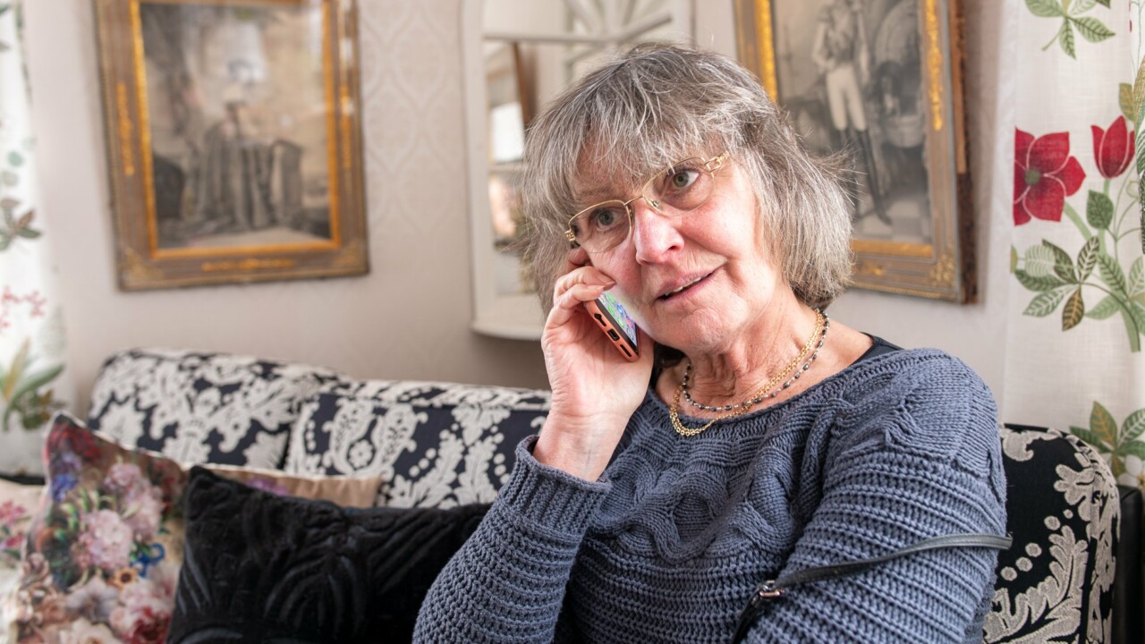En äldre kvinna sitter i soffan och pratar i sin smartphone