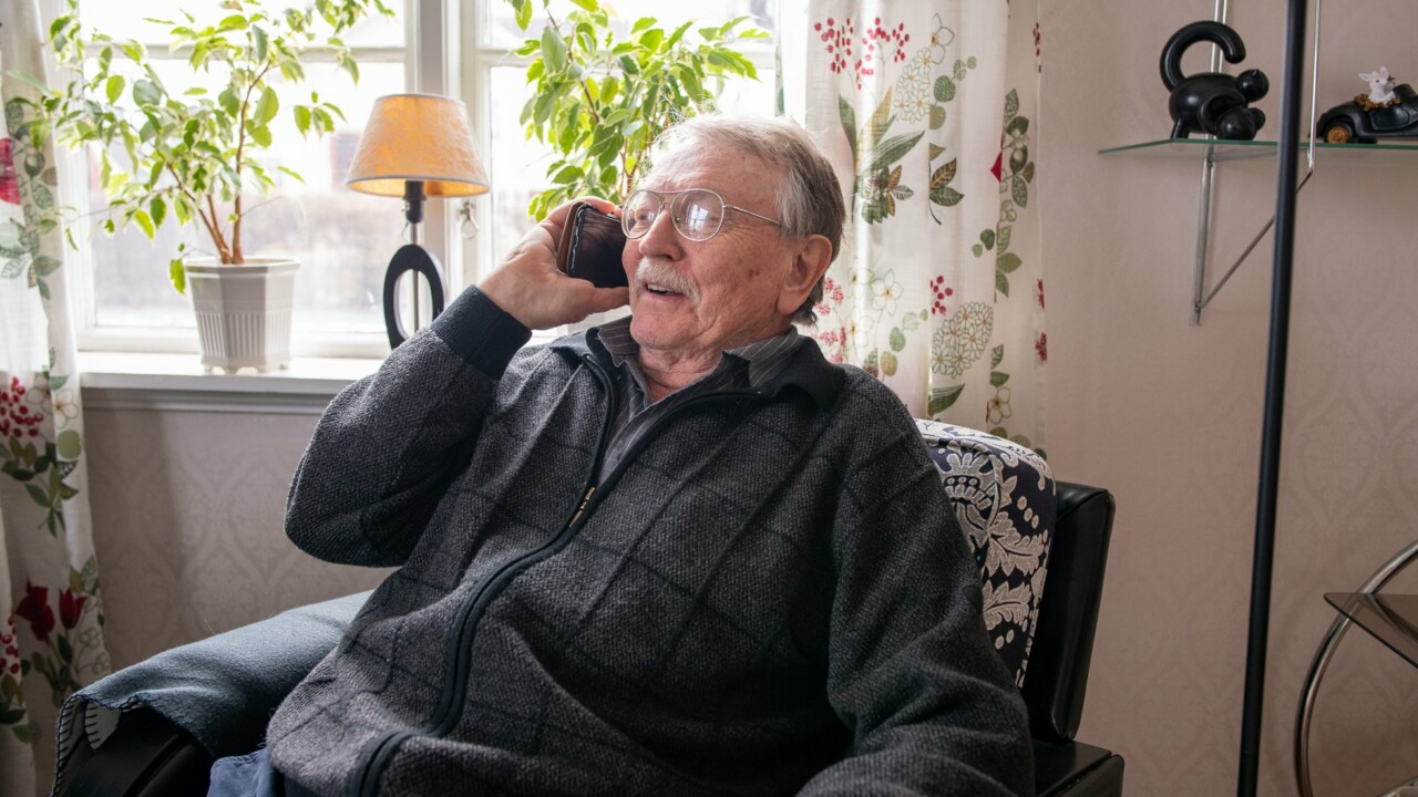 Äldre man sitter i en fåtölj och pratar i sin smartphone