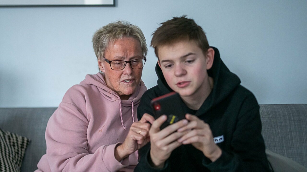 En äldre kvinna tittar på en smartphone tillsammans med en ung kille.