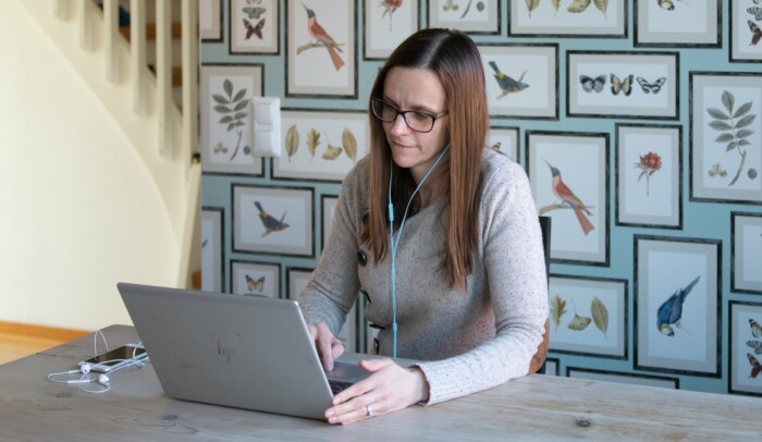 Kvinna sitter hemma vid ett skrivbord och jobbar på laptop.