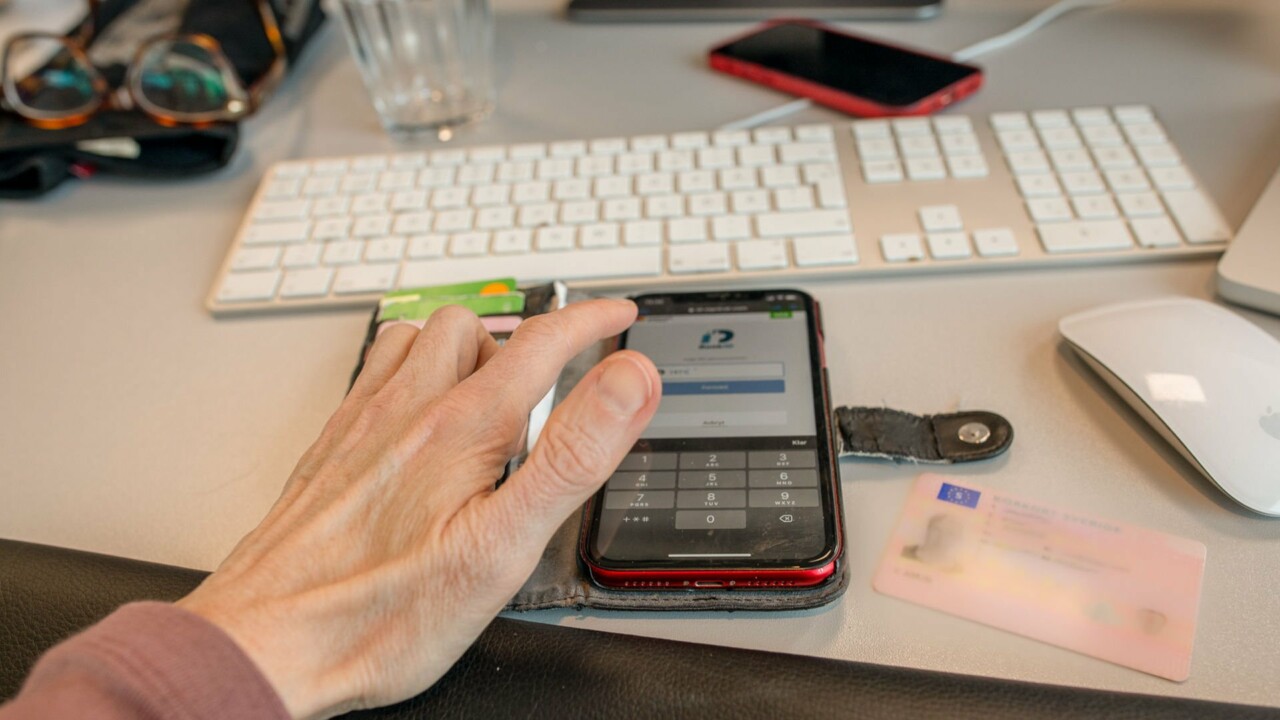 Händer vid mobiltelefon, på skärmen syns e-legitimation och på bordet ligger ett körkort.