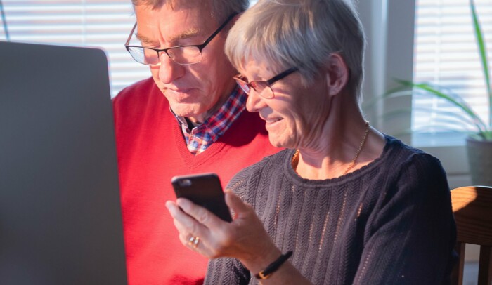 Man och kvinna sitter framför en dator, kvinnan har en mobil i handen.