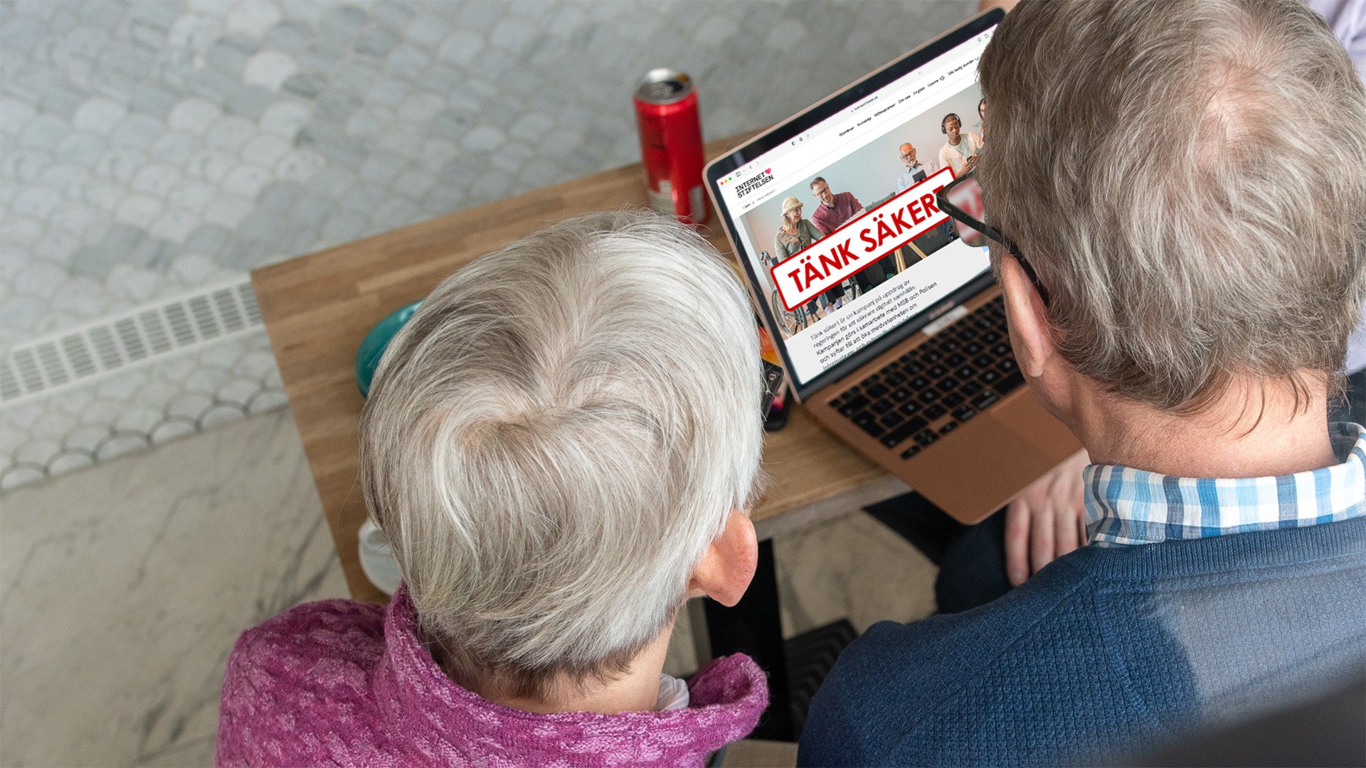 Äldre par sitter framför en dator, på skärmen syns Tänk säkert-kampanj