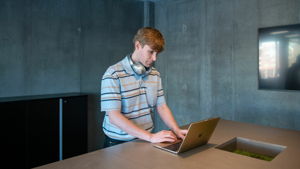 En man står vid ett bord med sin laptop framför sig.