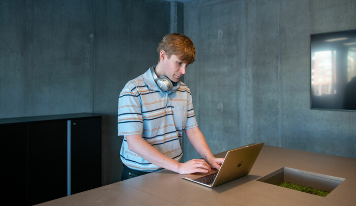 En man står vid ett bord med sin laptop framför sig.