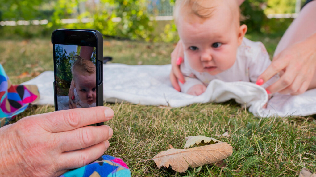 En kvinna tar bild på en bebis som ligger på en filt i gräset.
