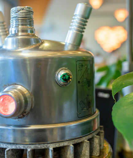 Ansiktet på en robot, roboten är i plåt med gröna lampor som ögon och en röd lampa som mun.