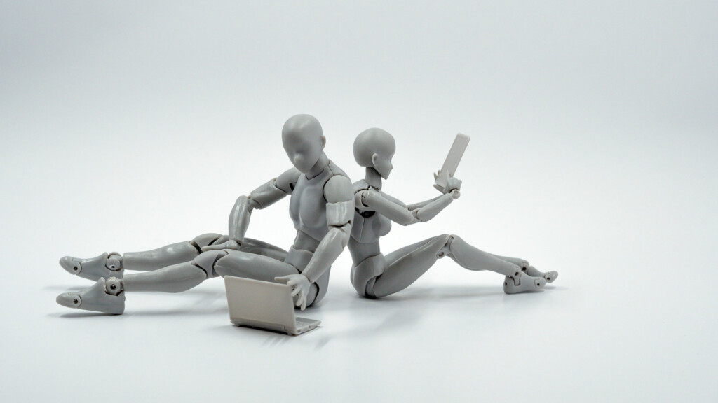 Två robotar sitter rygg mot rygg med varsin laptop.