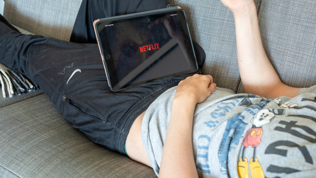 En ungdom ligger på en soffa med Ipad på magen, på skärmen syns Netfilx-loggan.