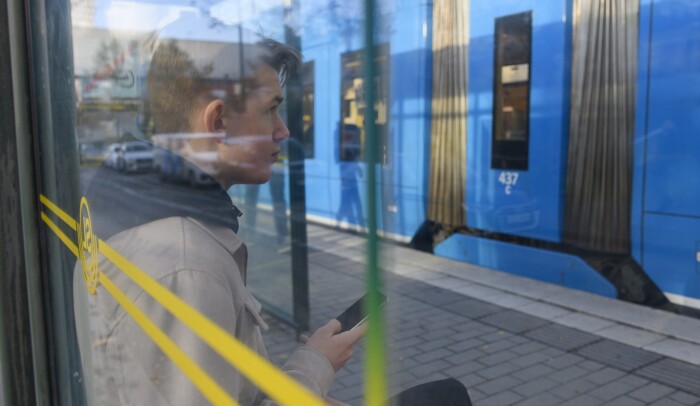En ung kille sitter i en kur vid tvärbanan och tittar på sin mobil.