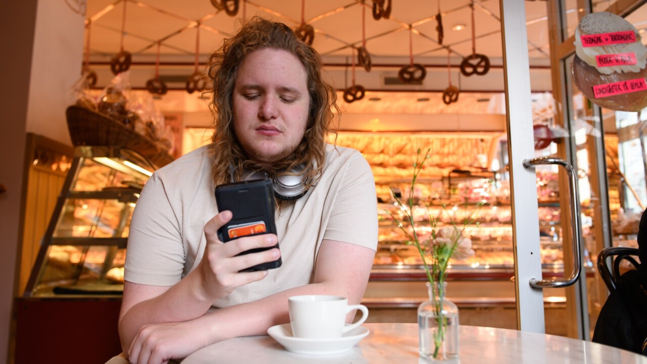 En man sitter vid ett bord på ett café och tittar på sin mobiltelefon.