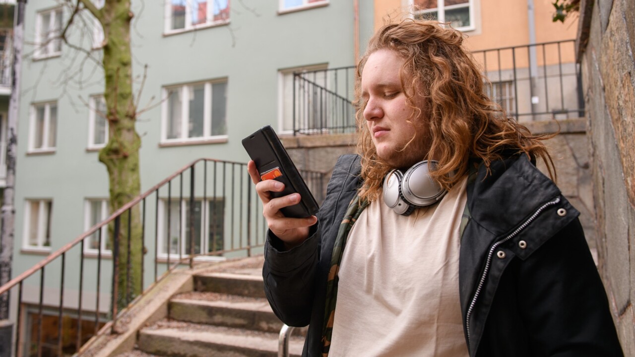 En man med hörlurar tittar på sin mobiltelefon.