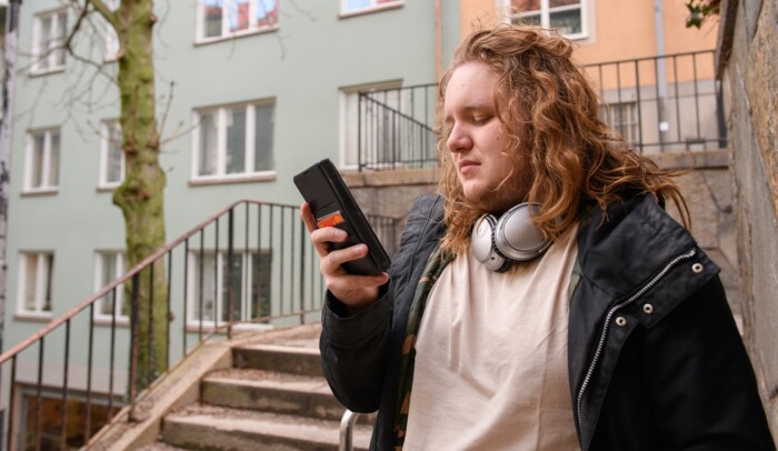 En man med hörlurar tittar på sin mobiltelefon.