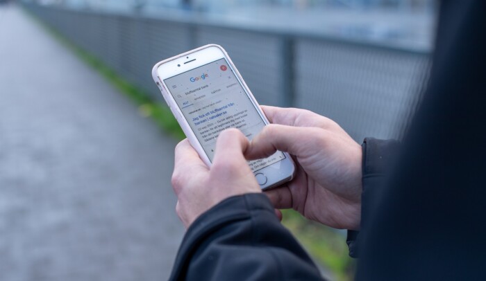 Händer som håller i en mobil, på skärmen syns sökmotorn Google.