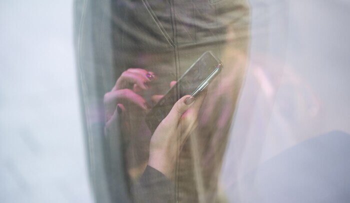 Reflektion av kvinnas händer som använder mobiltelefon.