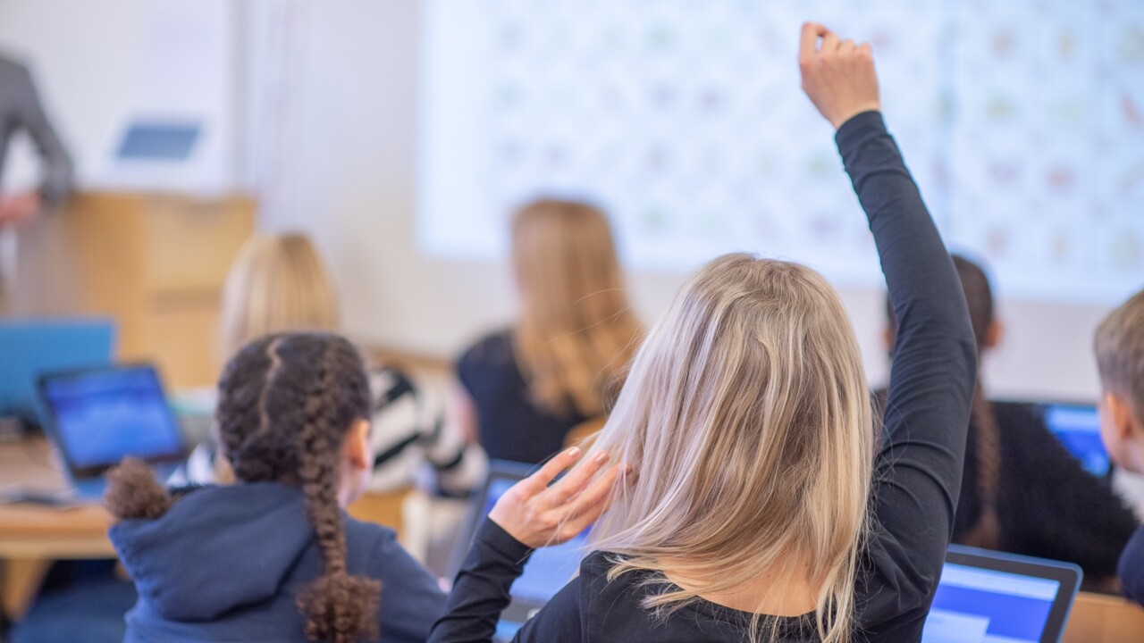 Ett klassrum fullt av elever som sträcker upp händerna i luften.