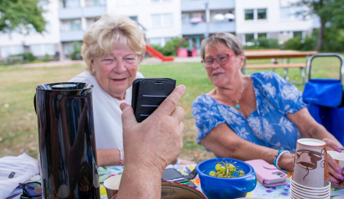 Två äldre kvinnor tittar på en mobilskärm som någon annan håller upp framför dem, de är utomhus.