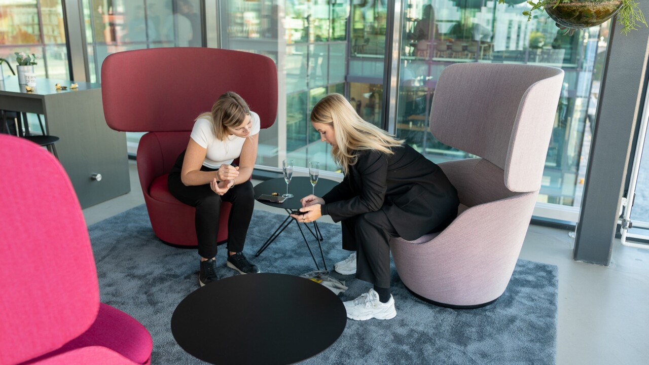 Två kvinnor som sitter i ett rum bredvid varandra och tittar på en mobiltelefon.