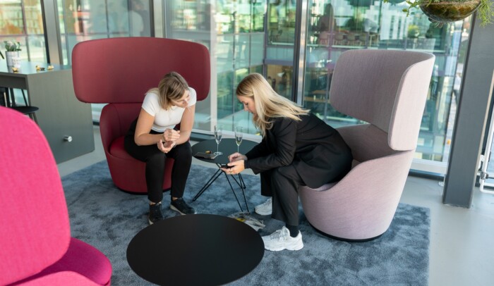 Två kvinnor som sitter i ett rum bredvid varandra och tittar på en mobiltelefon.