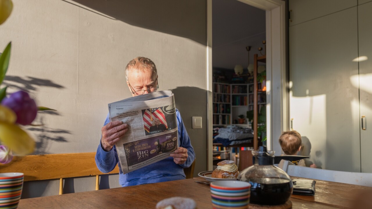 En man sitter i ett kök och läser en tidning.