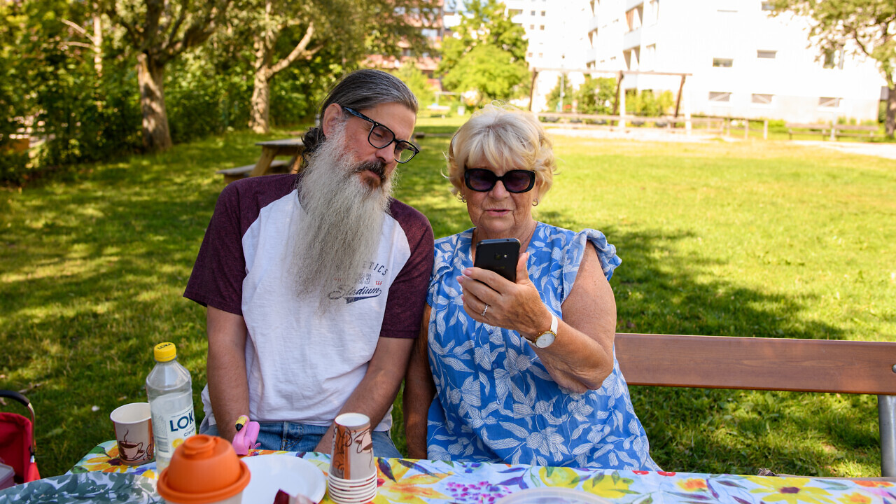 Två personer sitter utomhus och tittar på en mobiltelefon.