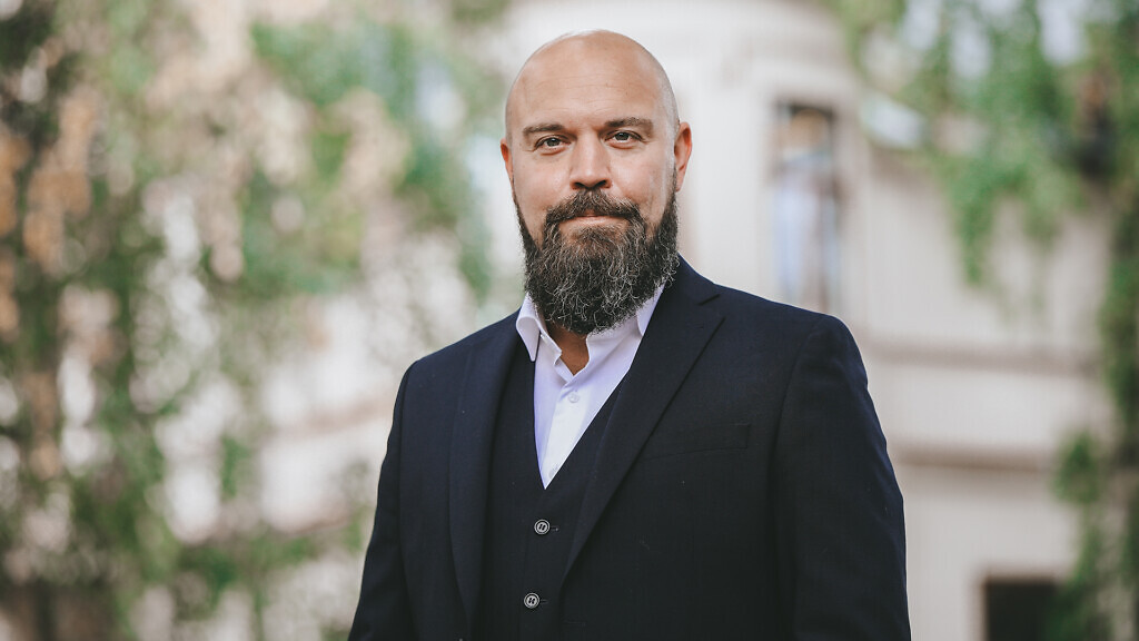 Porträtt av Conny Sohlberg, som står i kostym framför en gammal byggnad