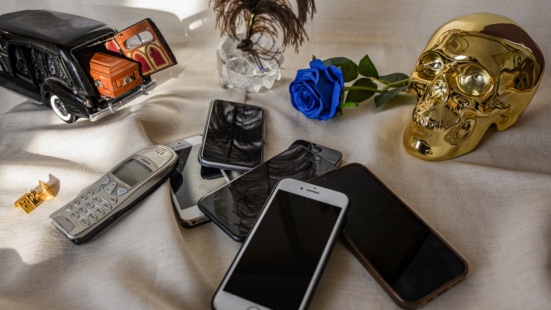 Mobiltelefoner, begravningsbil, döskalle och en blå ros på ett bord med vit duk.