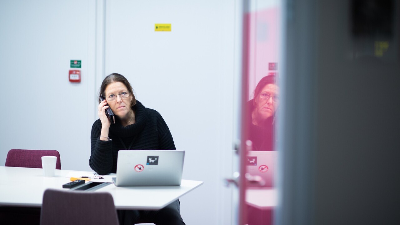 En kvinna sitter vid ett bord och pratar i mobiltelefon.