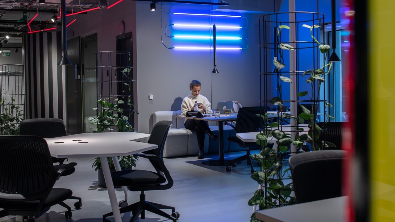 En kvinna sitter i en soffa på Goto10 Malmö och håller på med sin mobiltelefon. På bordet framför hene står en laptop.