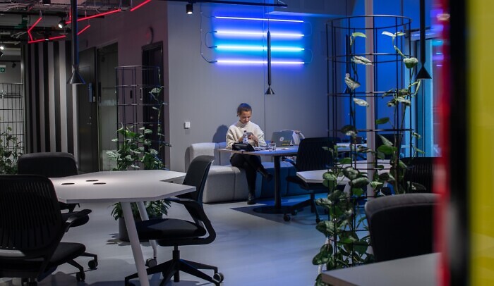 En kvinna sitter i en soffa på Goto10 Malmö och håller på med sin mobiltelefon. På bordet framför hene står en laptop.