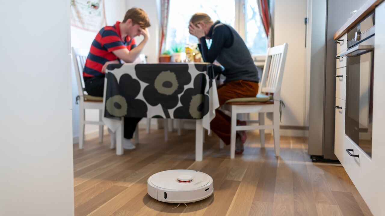 Två personer sitter vid ett bord med en robot på golvet.