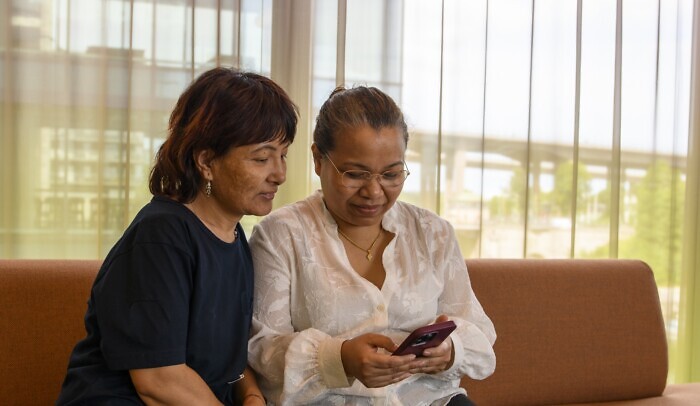Två kvinnor sitter i en soffa och tittar på en mobiltelefon.