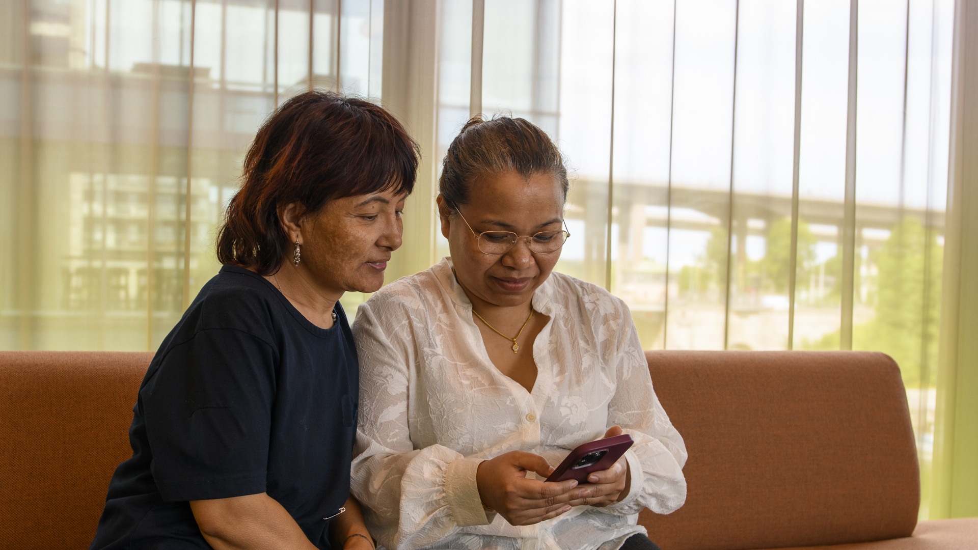 Två kvinnor sitter i en soffa och tittar på en mobiltelefon.