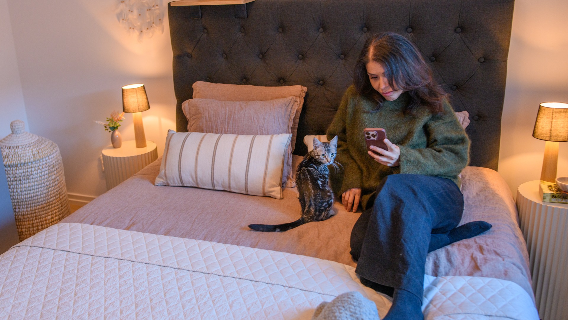 En kvinna sitter på en säng och tittar på sin telefon.